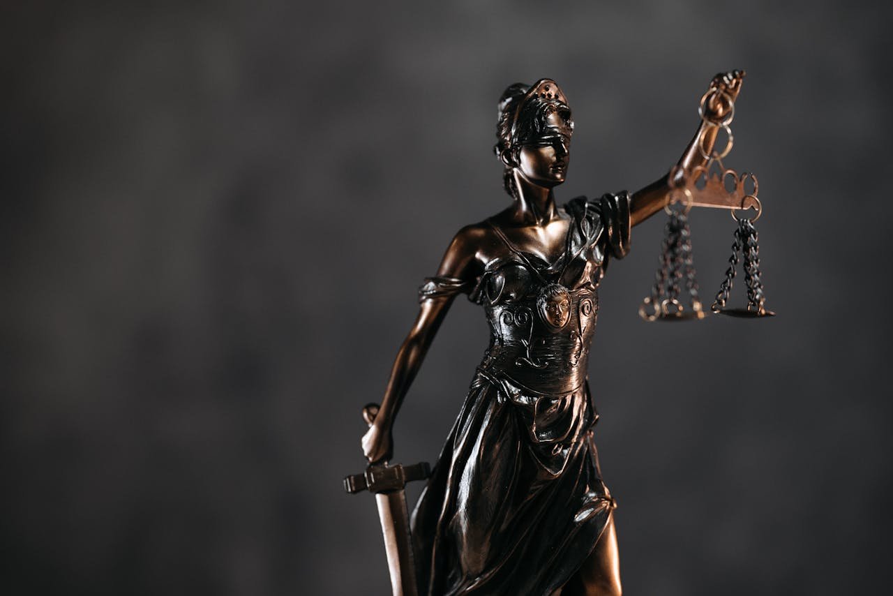about-02 Detailed bronze Lady Justice statue with scales and sword against a dark background, symbolizing law and justice.